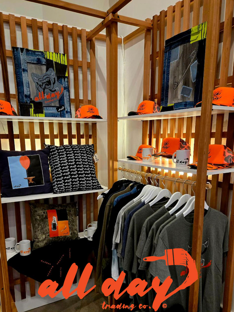 Display of clothing and accessories with 'all day trading co' branding in a store setting.