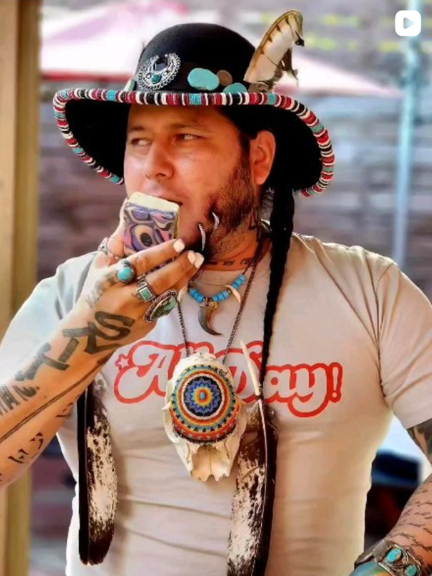 Person wearing a colorful hat and All Day t-shirt, holding a can, with a blurred background