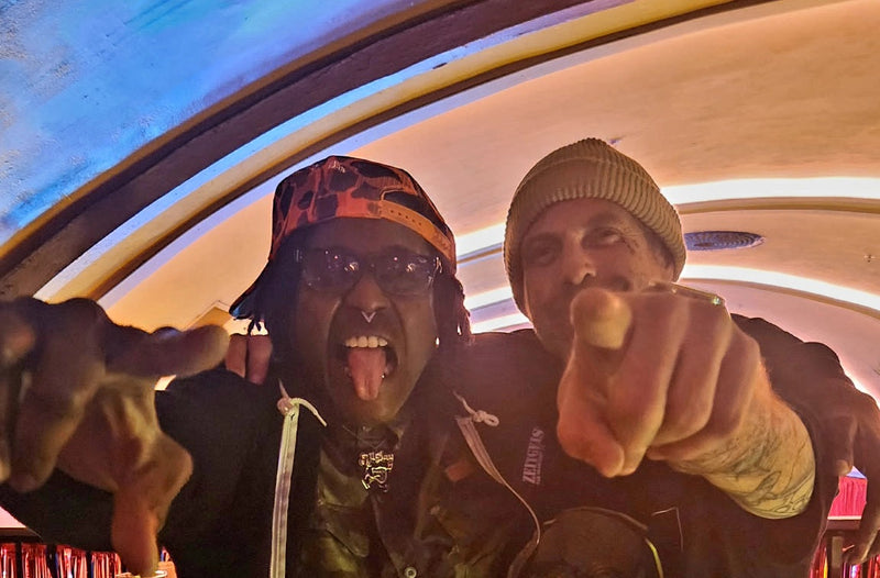 Two people making a peace sign gesture indoors with colorful lights in the background