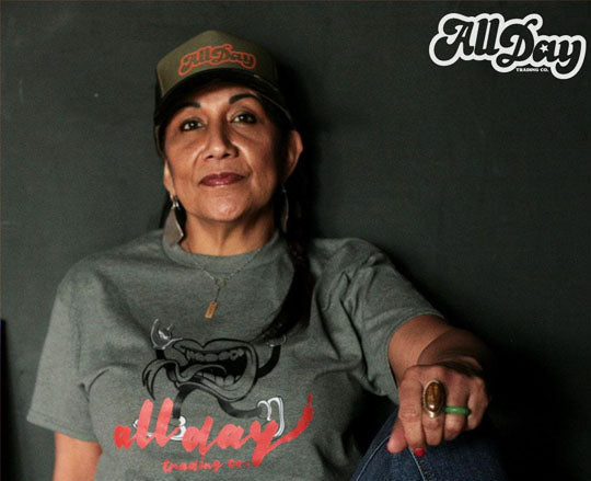 Person wearing a gray 'All Day' t-shirt and cap against a dark background