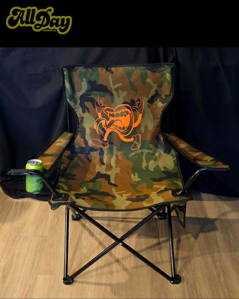 Camouflage folding chair with orange logo on a wooden floor, branded 'All Day'.