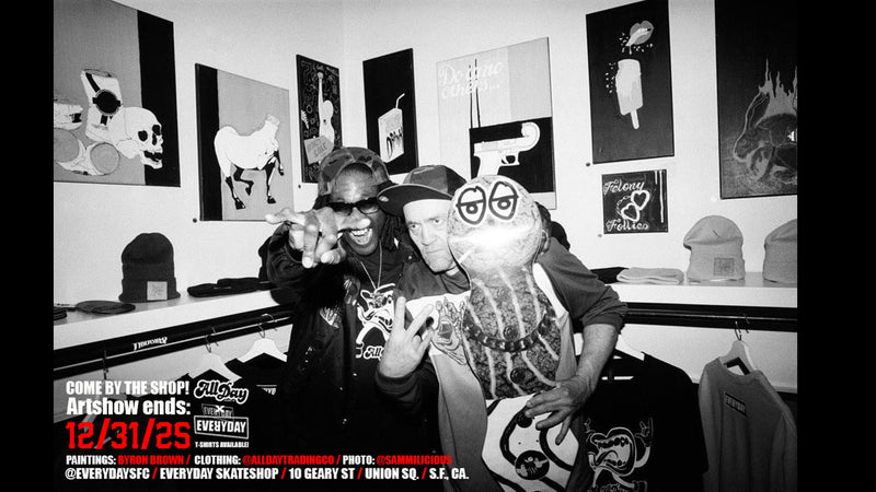 Two people posing with a skeleton mascot in a room with art on the walls.